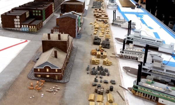 A diorama is under construction depicting buildings, people, livestock, cargo, and steamboats, allowing visitors to experience the historic riverfront era before the Gateway Arch.